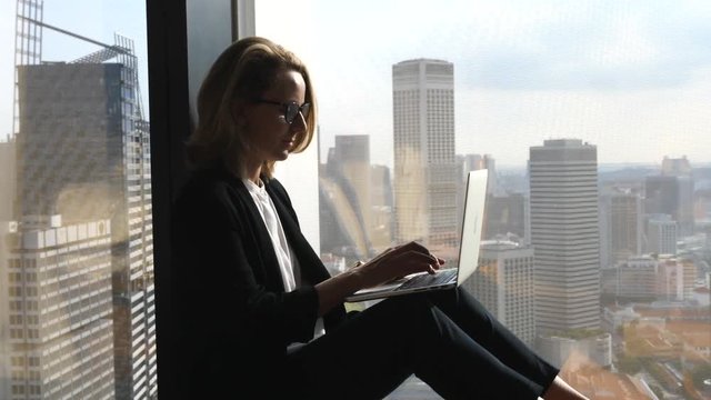 Business Woman Using Laptop Computer Sitting At Office Window With City View