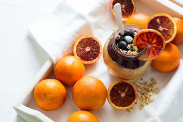 Jar of fresh smoothie with orange, blueberry and granola on white wooden salver