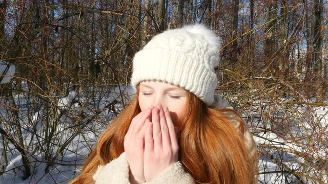 Ginger-haired girl is breathing on his frozen hands in the cold