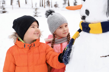 Happy children making snowman in park on winter vacation