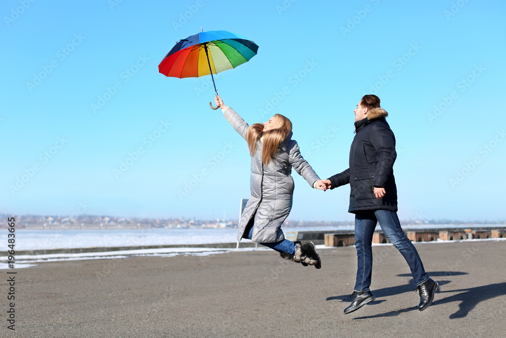 Wall mural Young romantic couple with colorful umbrella on river bank