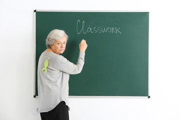 Senior teacher with paper fish on her back writing on chalkboard. April fool's day celebration
