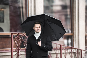 Young man in warm clothes with dark umbrella outdoors