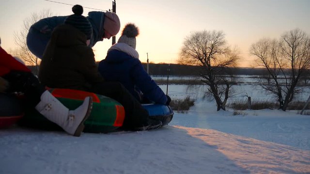 Winter vacation: kids riding on inflatable snow tube from a hill. Children climb the hill, carrying a sled. Winter, active rest.
