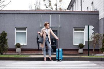 businesswoman with suitcase and umbrella waiting for taxi on street