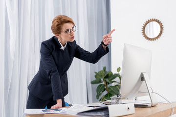 businesswoman pointing away while arguing with colleague at workplace in office