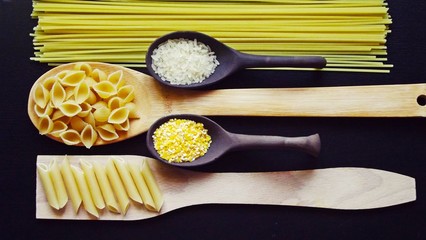 Cereals and pasta in spoons on black background.