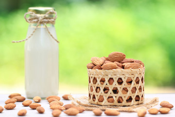 Almonds seed in wooden basket and Almonds milk in glass bottle on natural green background