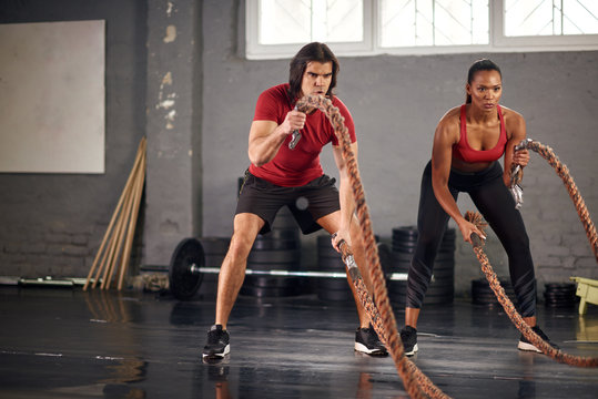 Man and woman working out with ropes in gym