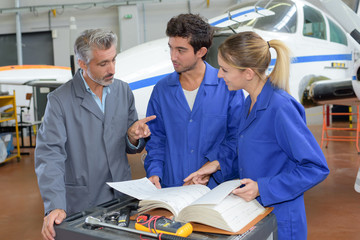 People looking at book in aircraft hangar