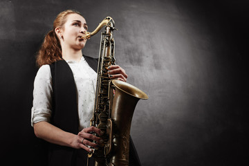 Young woman with saxophone on black background