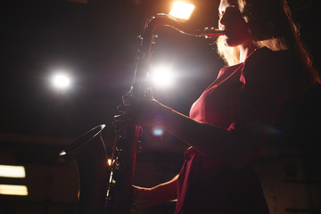 Musician girl in a red dress with a saxophone on stage