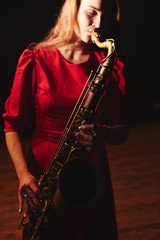 Musician girl in a red dress with a saxophone on stage