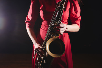 Musician girl in a red dress with a saxophone on stage