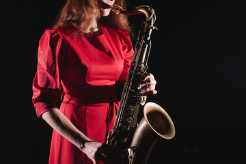 Fototapeta na wymiar Musician girl in a red dress with a saxophone on stage