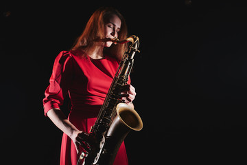 Obraz na płótnie Canvas Musician girl in a red dress with a saxophone on stage