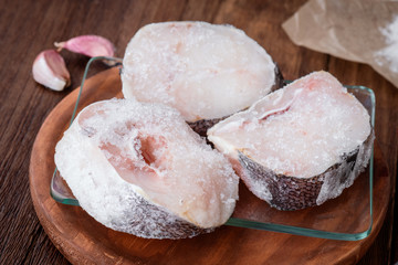 raw hake wheels frozen in glass tray on wood