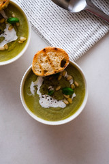 Spring detox broccoli green cream soup in bowls over marble background, top view. Clean eating, dieting, vegan, vegetarian, healthy food concept