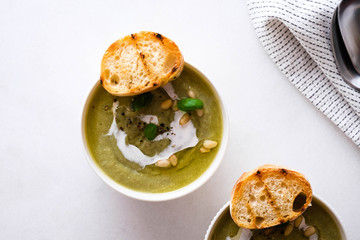 Spring detox broccoli green cream soup in bowls over marble background, top view. Clean eating, dieting, vegan, vegetarian, healthy food concept