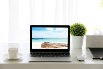 Fototapeta premium Beach in screen Laptop on table and Coffee cup room Office morning.concept of time relax.