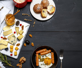 fried egg and sausages in a black crockery cast-iron frying pan, pieces of  cheese