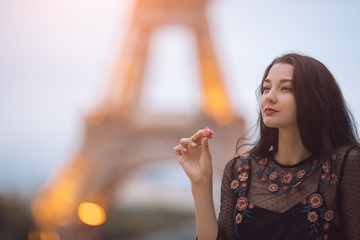 Paris woman smiling eating the french pastry macaron in Paris. Evening Eiffel tower with lights in the background. Portrait of gorgeous romantic young sensual girl in fashion black sexy dress enjoying