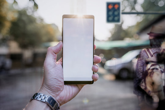 Hand man holding smartphone with blank white screen with blurred image of traffic light