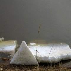 Big melting pieces of spring snow on the river beach water background