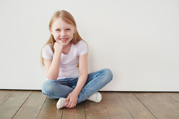 Portrait of a little girl sitting on a wooden floor near a white wall