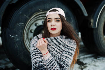 Brunette stylish casual girl in cap sitting against truck wheels.