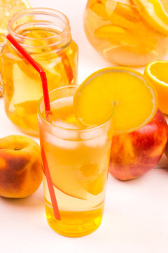 Apples, peaches, lemon and orange and a refreshing fruit juice with ice in a glass