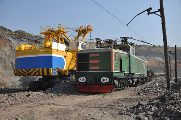 The excavator loads wagons with iron ore into the wagons. Electric locomotive with wagons.