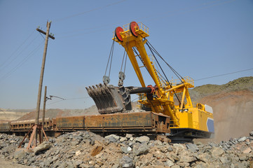 A large yellow excavator loads ore into a railway car