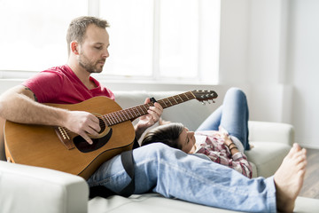 Young couple sitting on sofa in living room and playing guitar