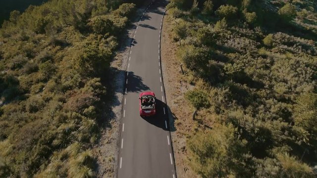 Aerial drone footage of camera following small red convertible car european cabriolet style, riding through empty secluded mountain road, exploring new travel tourist destination on amazing blogger