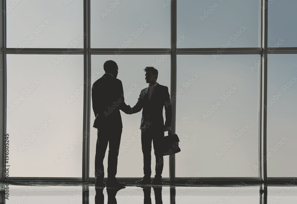 Wall mural silhouette view of two young businessmen are standing in modern office with panoramic windows