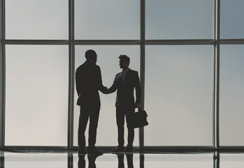 Silhouette view of two young businessmen are standing in modern office with panoramic windows