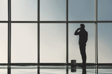 Fototapeta na wymiar Silhouette view of young businessman is standing in modern office with panoramic windows