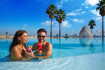 Tourist couple having bath in infinity pool on a beach resort with cocktails