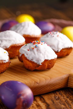Easter still life with cupcakes in white glaze and unusually colored yellow and purple eggs on a wooden background.