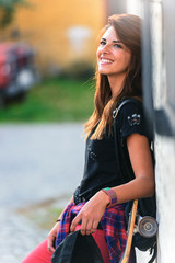 Beautiful smiling young woman skater with a long board standing in the street