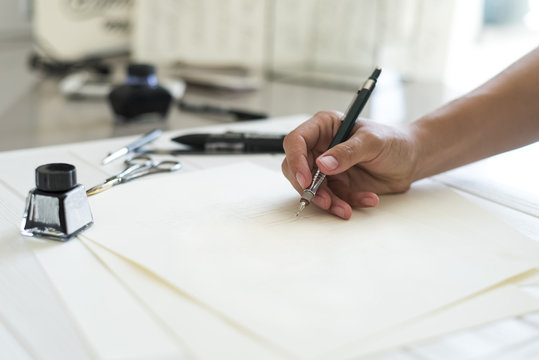 Designer's hand wrighting logo. Design studio. Designer's attributes on table: scissors, pencil, pen etc. 