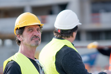 Absorbed and pensive construction worker wearing yellow reflective vest and hardhat looking away