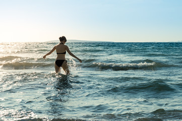 Fototapeta na wymiar Young, slim, sexy Caucasian woman black bikinis walking in the sea with splashes
