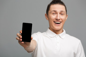 Cheerful young man standing isolated showing display of mobile phone.