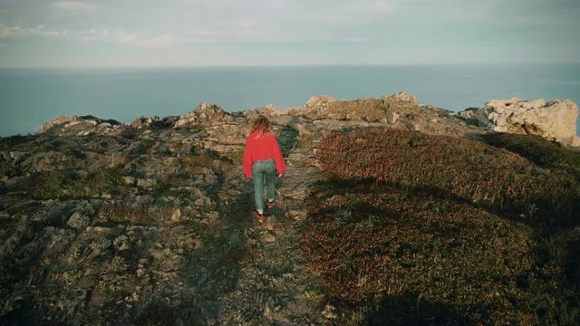 Cute petite young blonde woman in bright red sweater walks through rocks an cliffs on small mountain trail with best friend dog. concept adventure, nomad, travel blogger and influencer in nature