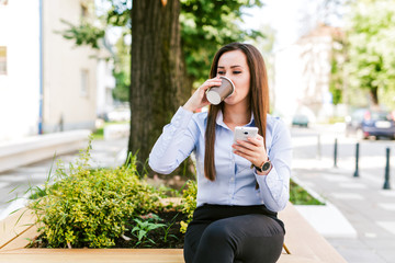 Young beautiful businesswoman drinks coffee and use cellphone