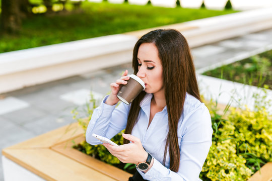 Young beautiful businesswoman drinks coffee and use cellphone