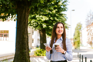 Fototapeta premium Young beautiful businesswoman drinks coffee and use cellphone