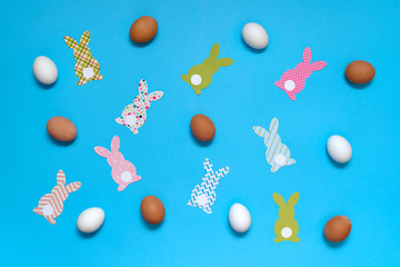 Fototapeta na wymiar Easter bunny decoration and eggs on blue background, copy space. DIY holiday handicraft of colorful rabbits. Flat lay, top view. Paper rabbits cutouts. Easter greeting card. Happy Easter concept